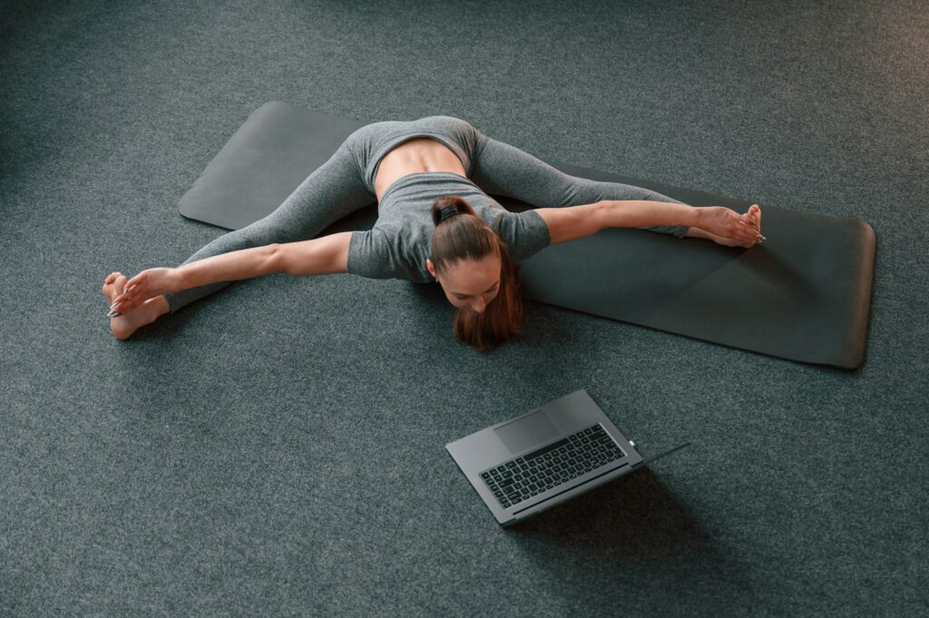 Taking online lessons by using laptop. Young woman in yoga clothes doing fitness indoors